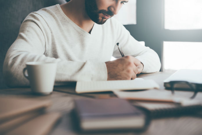 a man writing in a notebook at a desk
