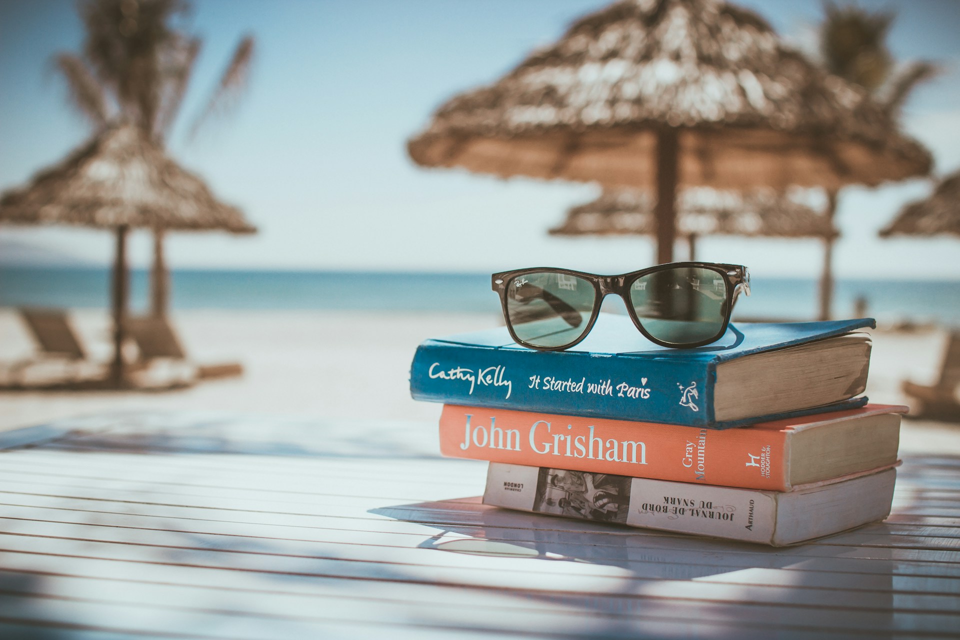 A pair of sunglasses on top of a pile of books, on a beach