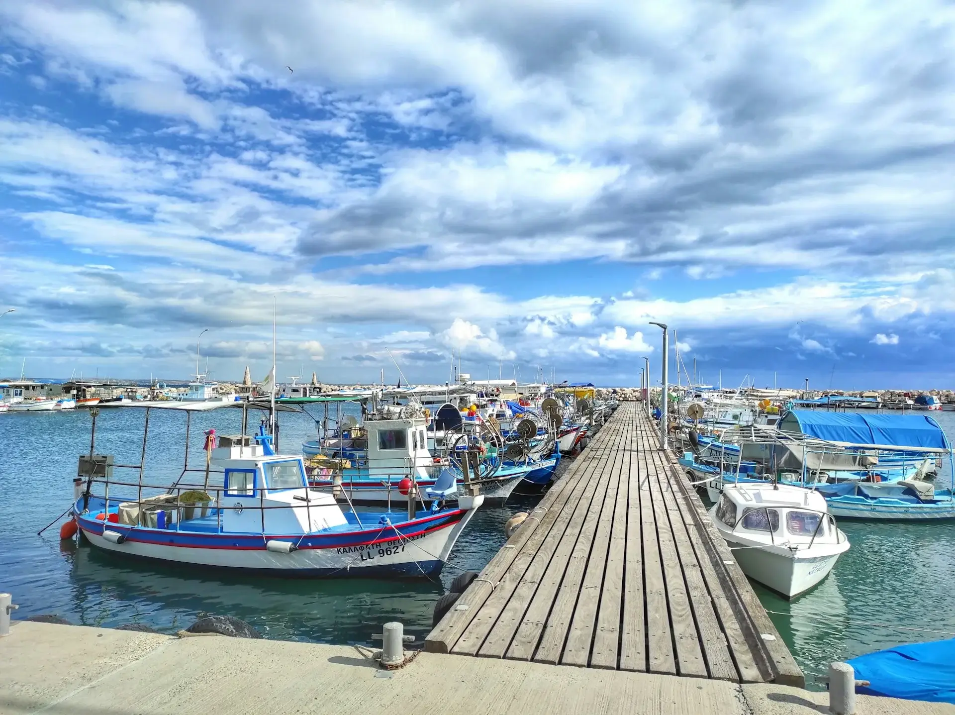 fishing boats moored against a jetty under a cloudy blue sky